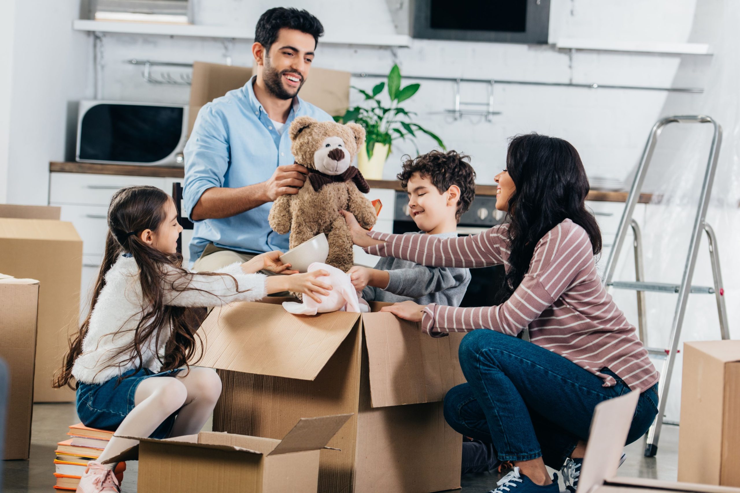 Cheerful latin father holding soft toy near hispanic family while unpacking boxes in new home